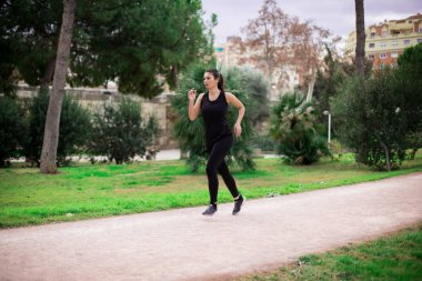 Güzel, genç, sportif bir kadın parkta spor kıyafetlerle koşuyor. Eğitim günü.