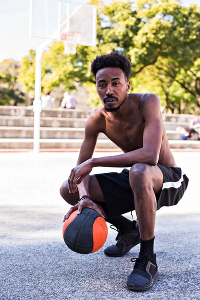 Young athletic black man posinging on court with ball, basketball game player, morning exercises, active healthy lifestyle, hot summer day, streetball.