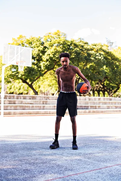 Young athletic black man posinging on court with ball, basketball game player, morning exercises, active healthy lifestyle, hot summer day, streetball.