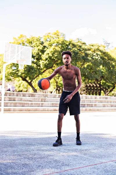 Young athletic black man posinging on court with ball, basketball game player, morning exercises, active healthy lifestyle, hot summer day, streetball.