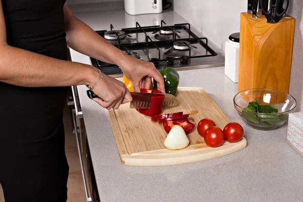 Wooden cutting board with vegetables and a knife, a woman cuts vegetables for salad.