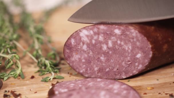 Saucisse savoureuse coupée au couteau sur une planche à découper à côté d'herbes — Video