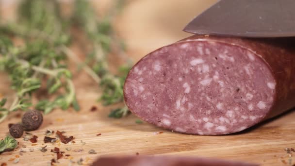 Fresh kielbasa being cutted with knife on cutting board next to herbs — Stock Video