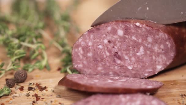 Свежая колбаса, нарезанная ножом на доске рядом с травами — стоковое видео
