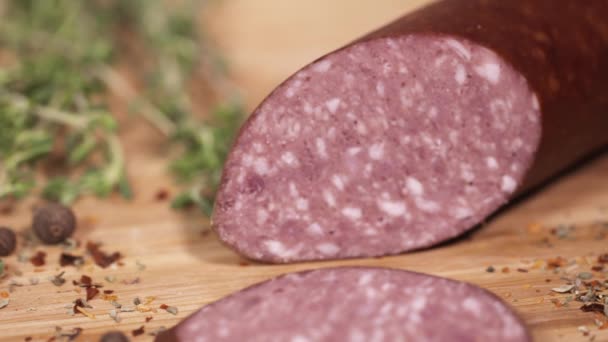 Tasty meat delicatessen being cutted with blade on cutting board next to herbs — Stock Video