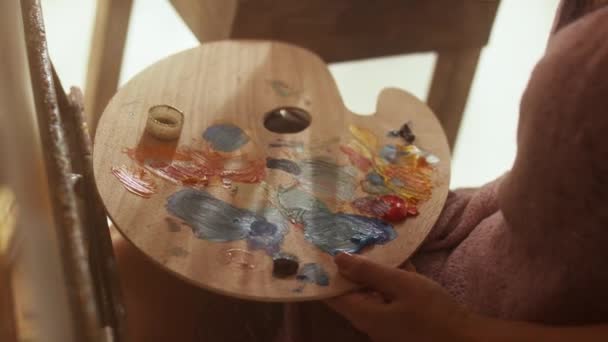 Mujer de mediana edad artista está pintando sobre lienzo sentado en estudio de arte de la luz del día — Vídeo de stock
