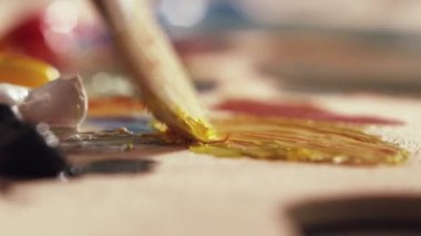 Sanatçı büyük boya fırçası ile palette farklı renkli yağlı boya karıştırma.