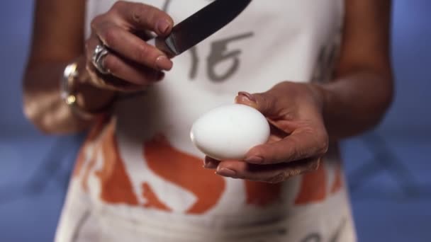 Woman wearing colorful apron is holding egg then breaking it with knife — Stock Video