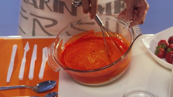 Handbesen mit orangefarbener und weißer Substanz in großer Glaspfanne auf weißem Tisch — Stockvideo