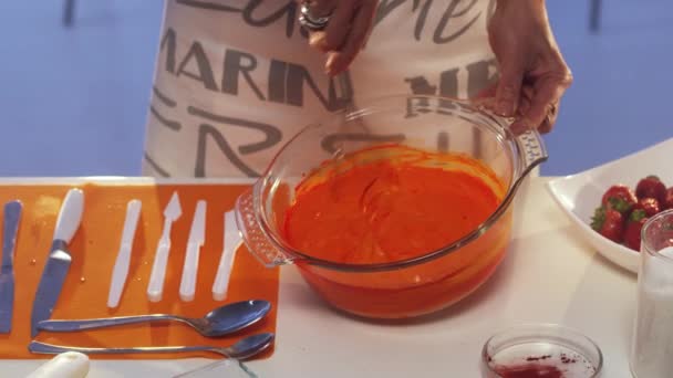 Womans hand is whisking orange substance in big glass pan on white table — Stock Video