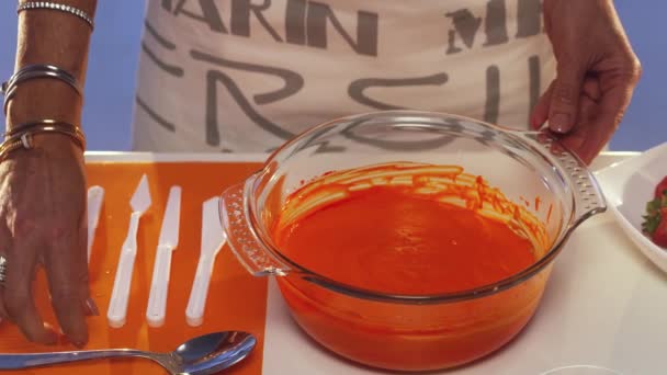 La mano de las mujeres está agitando sustancia naranja con cuchara en una sartén de vidrio grande en la mesa — Vídeo de stock