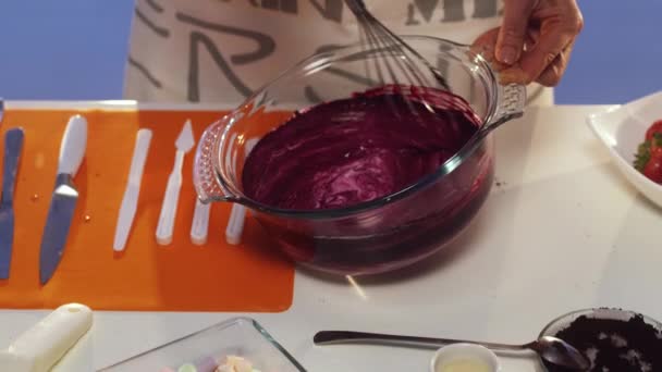 Ручное взбивание фиолетового вещества в большую круглую стеклянную кастрюлю на белый стол — стоковое видео