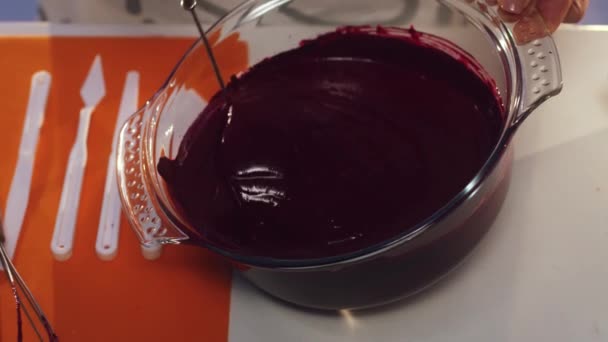 Frau in weißer und grauer Schürze verquirlt von Hand violette Substanz in großer Glaspfanne — Stockvideo