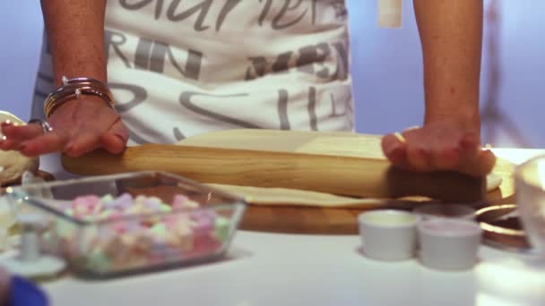 Женщина в фартуке выкатывает тесто на большой круглой деревянной доске со скалкой — стоковое видео