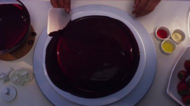Küçük yuvarlak pasta tarafından koyu mor krem kaplı iki farklı boy tabak dönen yerleştirilir ve eşit olarak beyaz kare düzeltti şeklinde plastik spatula ile diğer pişirme şeyler tabloda.