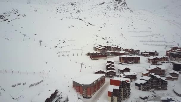 Камера дрона показывает современный, маленький, покрытый снегом горнолыжный курорт в окружении холмов — стоковое видео
