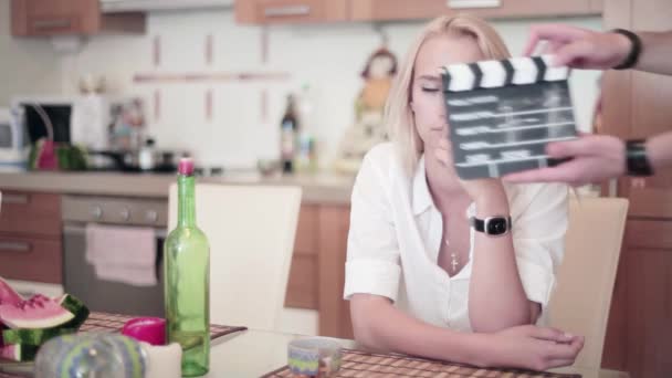 Διοικητικό Συμβούλιο Clapper χειροκροτήματα μπροστά χαριτωμένο ξανθιά γυναίκα που κάθεται στο τραπέζι στην κουζίνα — Αρχείο Βίντεο