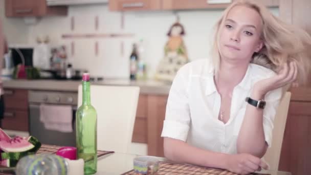 Joven hombre se une linda chica rubia vestida de blanco sentado en la mesa en la cocina — Vídeos de Stock