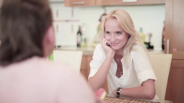 Atractivo rubio y joven vestido de blanco están sentados a la mesa en la cocina — Vídeos de Stock