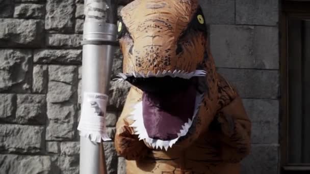 Person i t rex maskot står bredvid metall stuprör på staden gatan trottoaren — Stockvideo