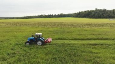 Viborg, Rusya Federasyonu - 11 Haziran 2018: Büyük mavi traktör yavaş yavaş alan yüzeyi kırmızı biçme makinesi eki ile biçiyor