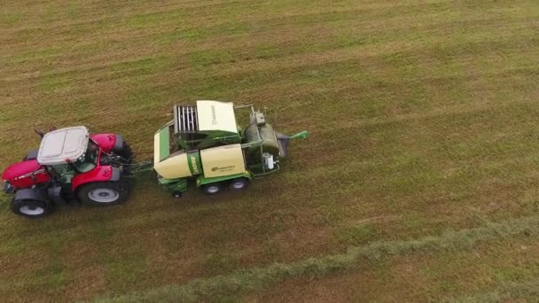 Viborg, Ryssland - 11 juni 2018: Kameran visar stora röda traktorn med bifogade funktionsdugliga gul hö balpress på fältet — Stockvideo