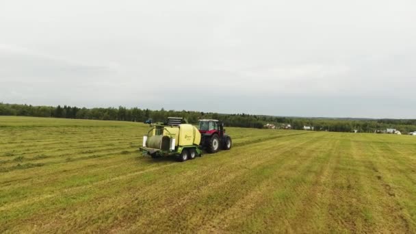 VIBORG, RUSSIE - 11 JUIN 2018 : La caméra attrape un gros tracteur rouge avec une presse à balles de foin jaune attachée se déplaçant sur le terrain — Video