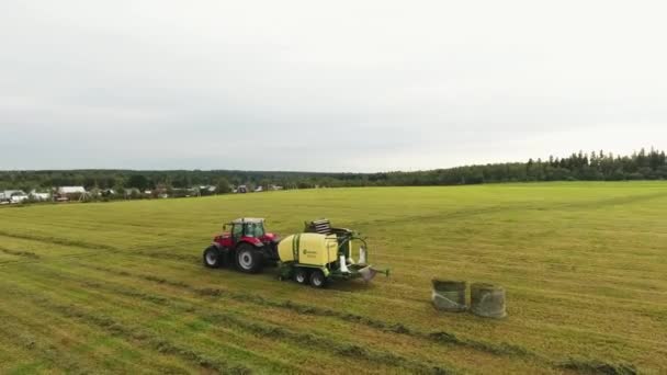 Viborg, Oroszország - 2018. június 11.: Kamera megmutatja piros traktor széna csomagoló mozog, maga mögött hagyva a bálázzák két mező — Stock videók