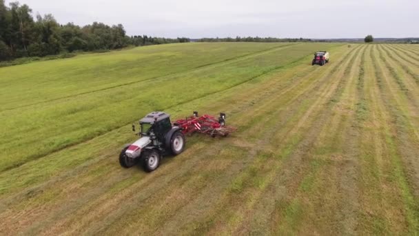 VIBORG, RUSIA - 11 DE JUNIO DE 2018: Vista de la cámara del dron del gran tractor gris en movimiento con rastrillos redondos rojos de trabajo — Vídeo de stock