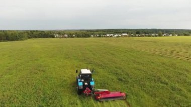 Büyük mavi traktör yavaş yavaş dikdörtgen kırmızı biçme makinesi ile yeşil alan biçiyor