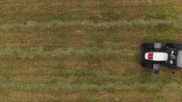 トップ ビューで実行している大きな灰色のトラクターのドローン カメラから区切られた赤の丸い形の大規模な緑の農地フィールドの表面に刈られた干し草をかき集めて耙の添付ファイル — ストック動画