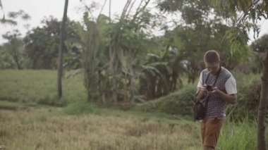 Kamera standları arasında tropikal çalılar ve ağaçlar, Genç adamla duman ve ateş.