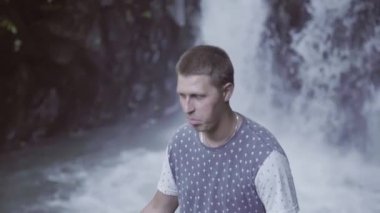 Küçük şelale önünde duran genç beyaz kısa saçlı adam.