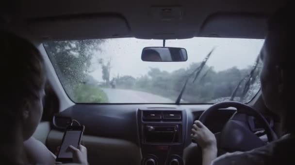 Кавказский мужчина и женщина сидят в машине и ездят по сельской дороге в дождливый летний день . — стоковое видео
