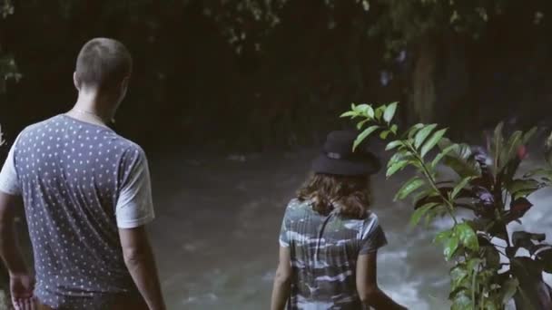 在森林中走向小瀑布的青年男女的背观 — 图库视频影像