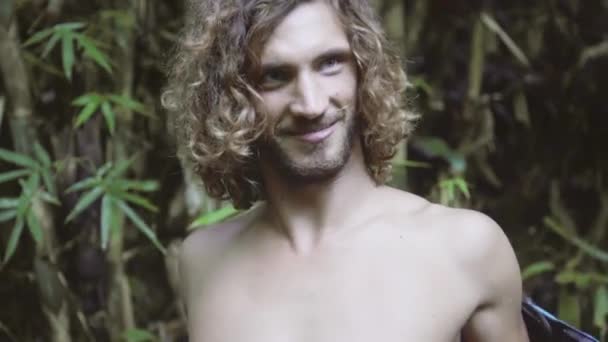 Attraktiver junger Mann mit langen lockigen Haaren zieht Rucksack vom nackten Rücken — Stockvideo