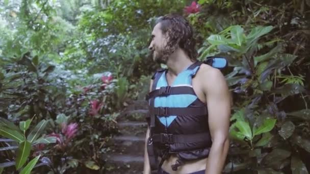 Cute young man with wet curly hair dressed in swim vest looks around and smiles. — Stock Video