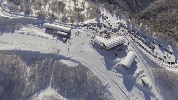 Vista aerea che mostra la stazione sciistica innevata piena di auto e persone nella giornata di sole — Video Stock