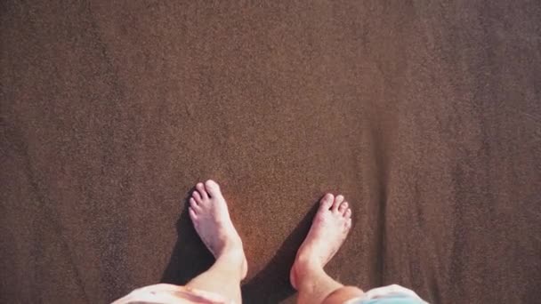 Bare feet sink and squish into the wet brown sand at the edge of coming waves — Stock Video