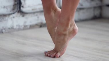 Kadın çıplak ayakları ısıtın ayakta ve ayak ucunda ahşap zemin üzerinde hareket ettirerek