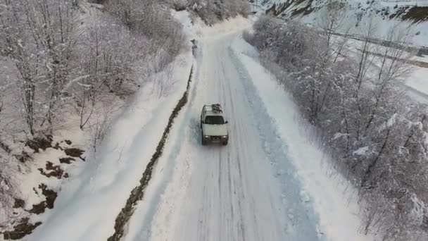 Bakuriani, Gruzie - 2. listopadu 2017: Velké bílé auto je jízda na zasněžené silnici mezi ojíněné stromy na zimní den — Stock video