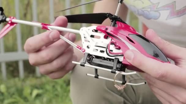 Weiße Herrenhand hält roten Nano-Hubschrauber und legt Ehering auf die Kufen — Stockvideo
