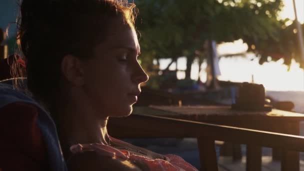 Portrait de jolie jeune femme assise sur une chaise longue à l'extérieur au coucher du soleil — Video