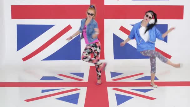 Две красивые женщины синхронно танцуют и прыгают на фоне британского флага — стоковое видео
