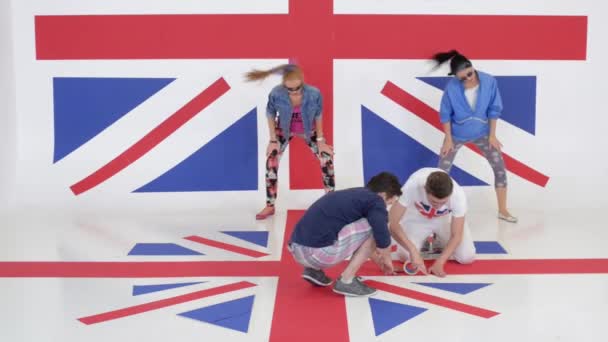 Dos chicas bailan sincrónicamente mientras dos tíos pegan piso con bandera británica . — Vídeos de Stock