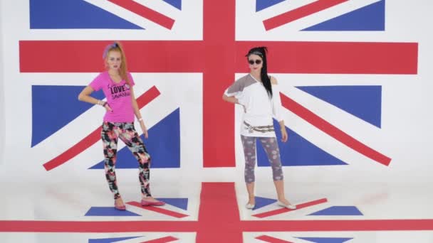 Ensayo de dos chicas lindas bailando sincronicamente sobre el fondo de la bandera británica — Vídeos de Stock
