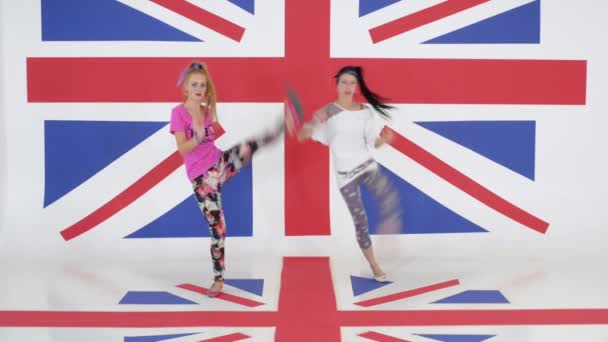 Ensayo de dos chicas simpáticas bailando sincronicamente sobre fondo de bandera británica — Vídeos de Stock