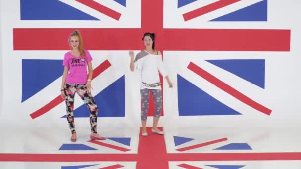 Репетиция двух харизматичных девушек, активно танцующих на фоне британского флага — стоковое видео
