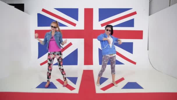 Две молодые улыбающиеся женщины активно танцуют на фоне британского флага — стоковое видео