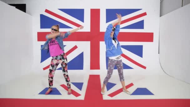 Dos hembras sonrientes jóvenes están bailando activamente en el fondo de la bandera británica — Vídeo de stock